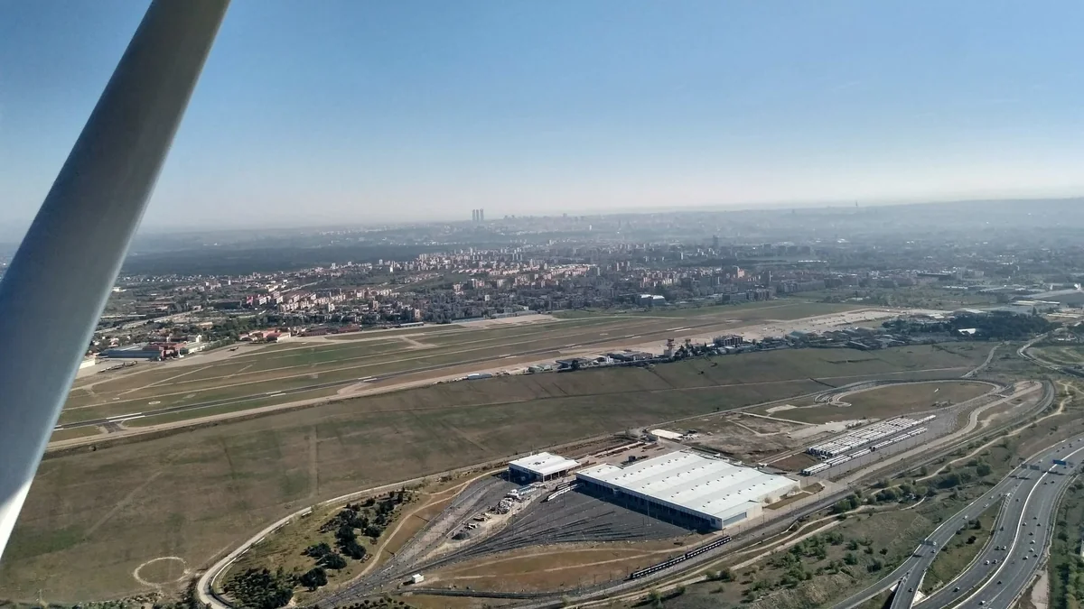 Aerial view of Madrid-Cuatro Vientos airport and the surrounding city from a light aircraft, with a wing strut in the foreground