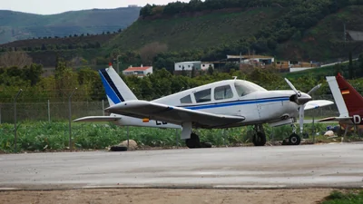 Una avioneta blanca y azul aparcada en el aeródromo de La Axarquía, en Vélez-Málaga, con colinas verdes detrás