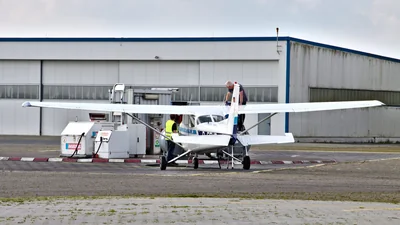 Cessna 172M being refuelled at a self-service fuel station on a grass airfield, with AvGas and MoGas tanks visible beside the wing