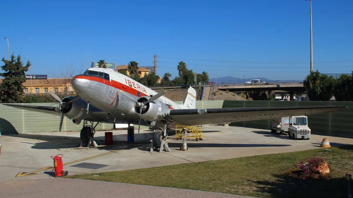 A silver Douglas DC-3 (C-47B) in Iberia livery with a red cheatline, registration EC-CPO, parked on the apron of the aviation museum at Málaga airport under a clear blue sky
