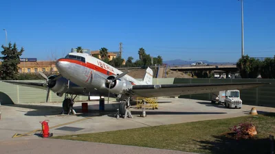 A silver Douglas DC-3 (C-47B) in Iberia livery with a red cheatline, registration EC-CPO, parked on the apron of the aviation museum at Málaga airport under a clear blue sky